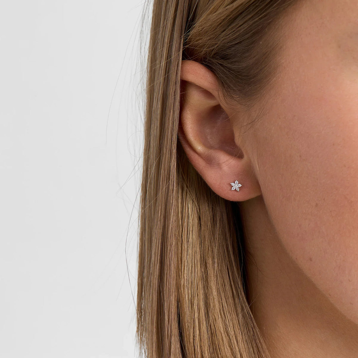 Ørestik i sølv med blomsterform og klare sten, vises på øre, forside