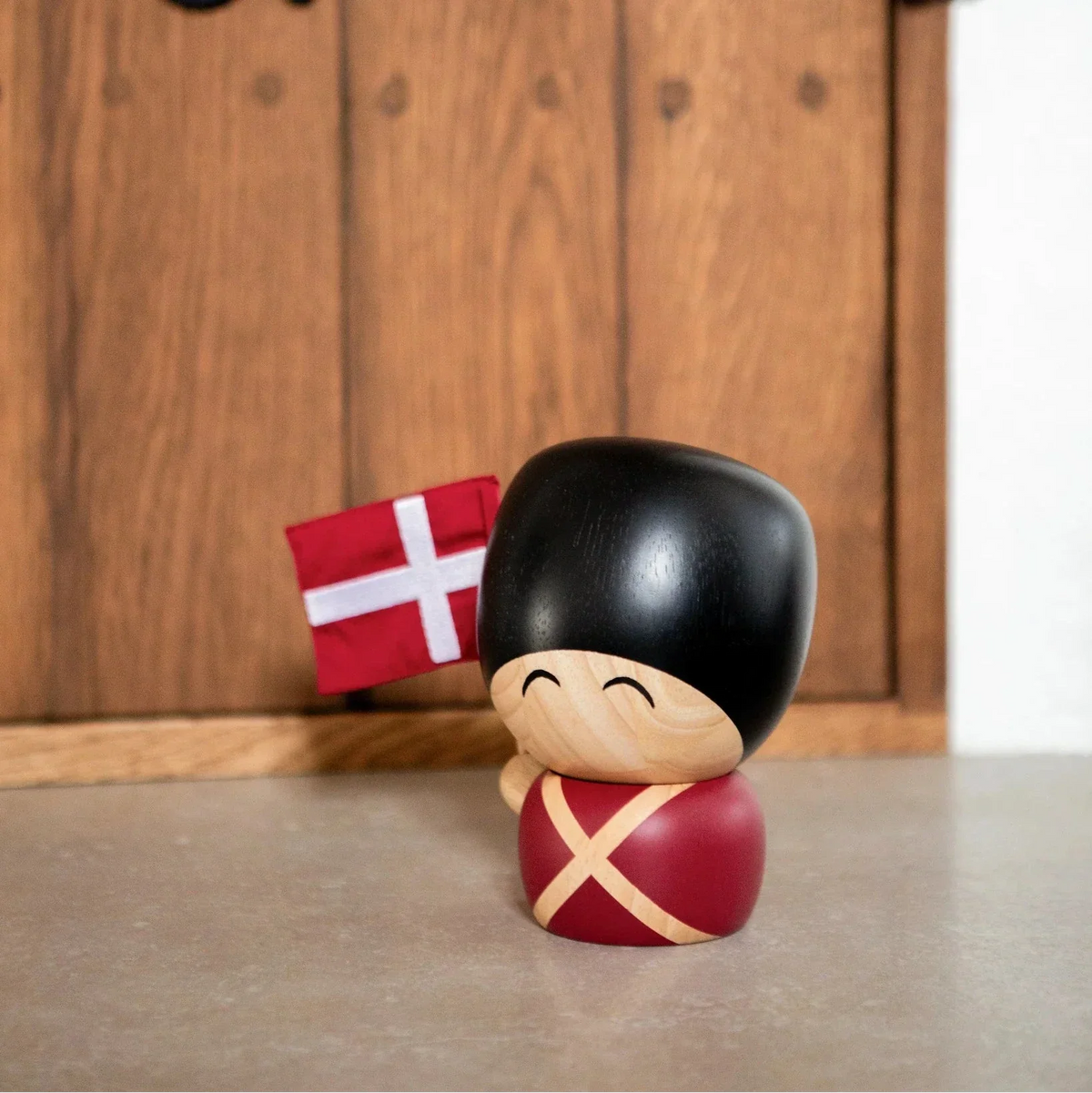 Kay Bojesen garder figur i træ med rød uniform og sort hat, holder Dannebrog, foran trædør. Model54428153889