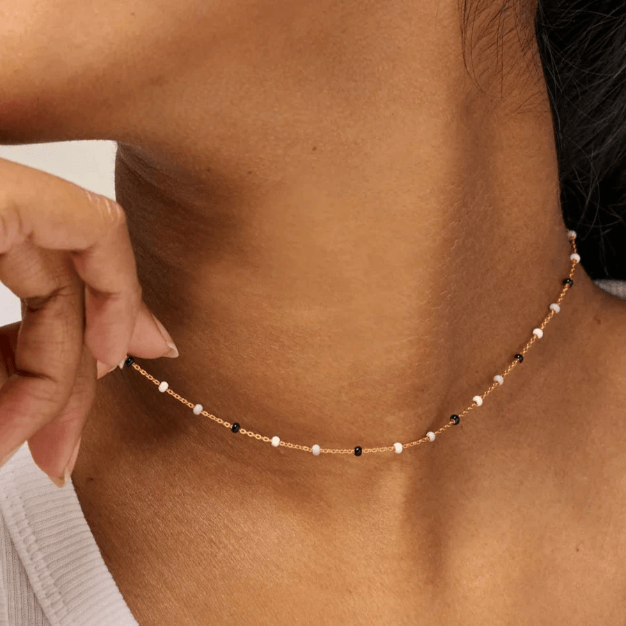 Enamel Lola Salt n Pepper Necklace vises om halsen på model, tynd kæde med små hvide og sorte perler. Model N55G-SALTPEPPER