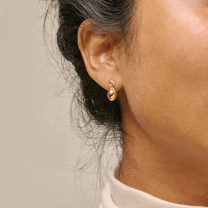 Enamel Poe Studs forgyldte øreringe bæres i øret, viser elegant dråbeformet gylden detalje. Model e385gm