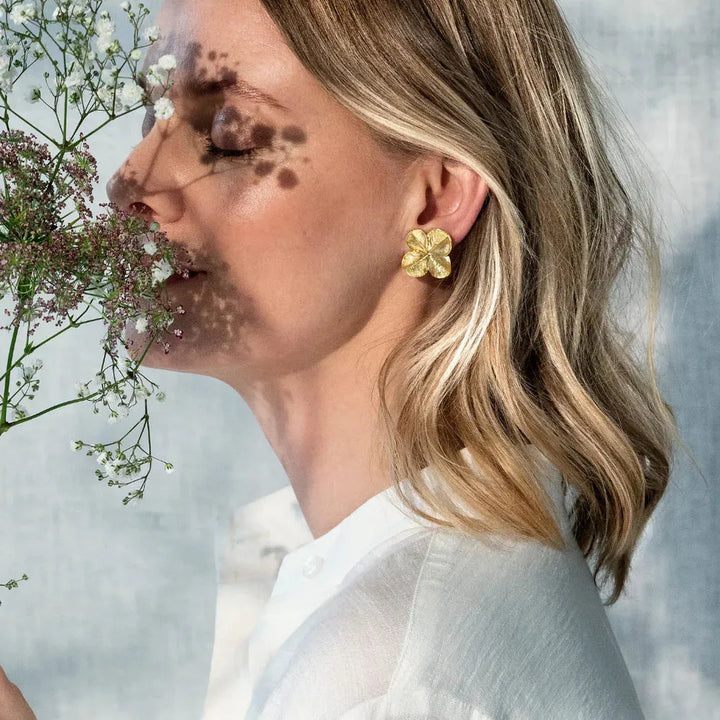 Flora Danica Firklover Ear Clips bæres af kvinde med korte lyse krøller, forgyldt blomstret detalje. Model 907-flc-eaclips-g-2