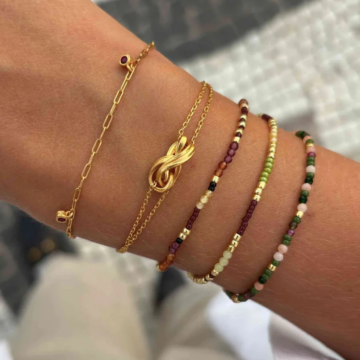 Hultquist Rowen Armbånd på håndled med gylden knude og farvede perlekæder i sollys. Model S08641G-2