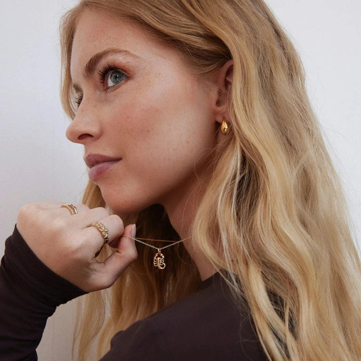 Jeberg I AM Zodiac halskæde forgyldt stjernetegn bæres af kvinde med bølget lyst hår. Model 42400-001.