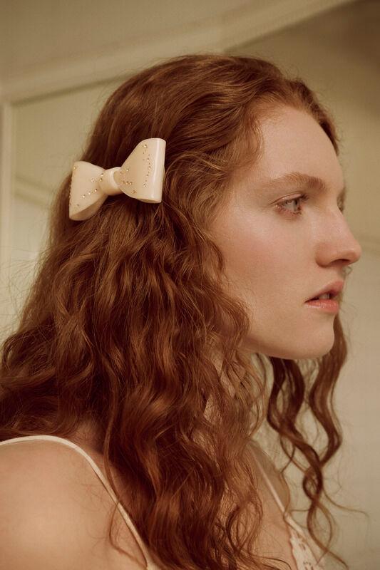 Maanesten Ribin Hair Clip Cream viser en cremefarvet hårklemme i sløjfeform på langt krøllet hår. Model 3981