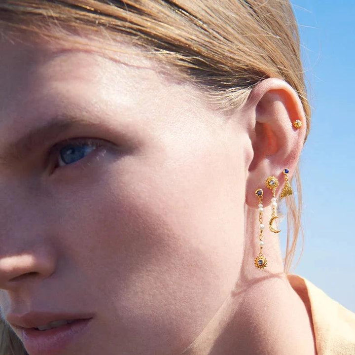 Maanesten Sunniva Earrings forgyldt vist på øre i sollys, elegante guld vedhæng og perle detaljer. Model 9717a-2
