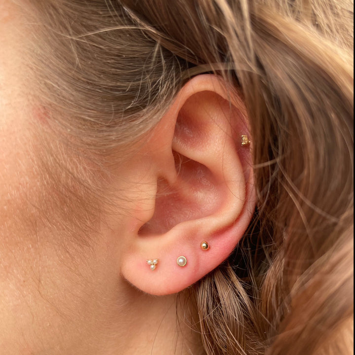 Maria Tash Natural Pearl Threaded Stud Earring 14kt vises i et øre, diskret ferskvandsperle på guld. Model xpe-yg-w2-001-2.