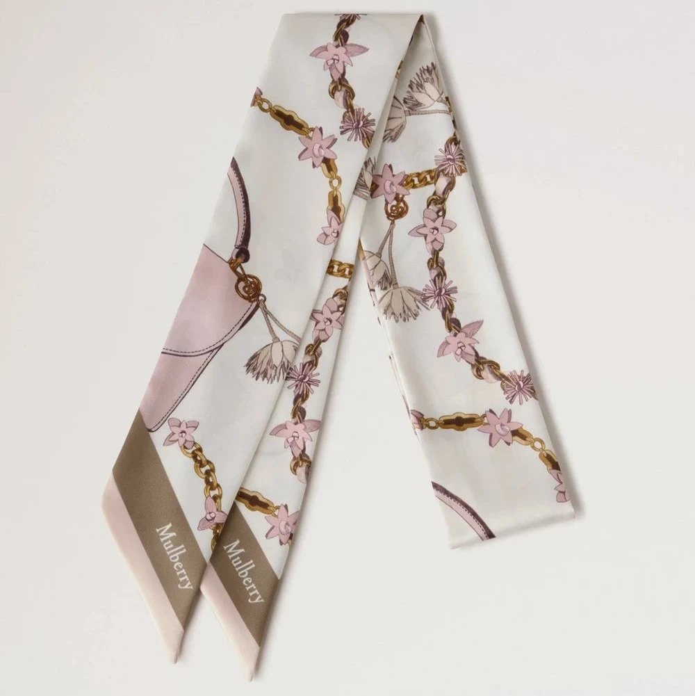 Mulberry Lana Bag and Chains Skinny Scarve Eggshell/Blossom Pink viser et smalt tørklæde i silke med lyserøde og gyldne kædedetaljer. Model VS4849115W569