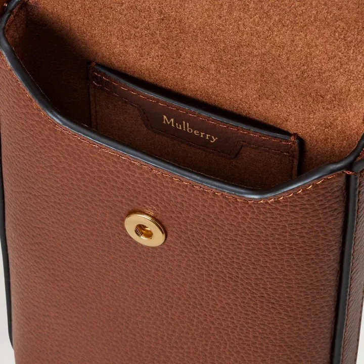 Mulberry Press Stud Phone Pouch oak viser nærbillede af brun læderoverflade og guldfarvet trykknap, Model RL9007552G110