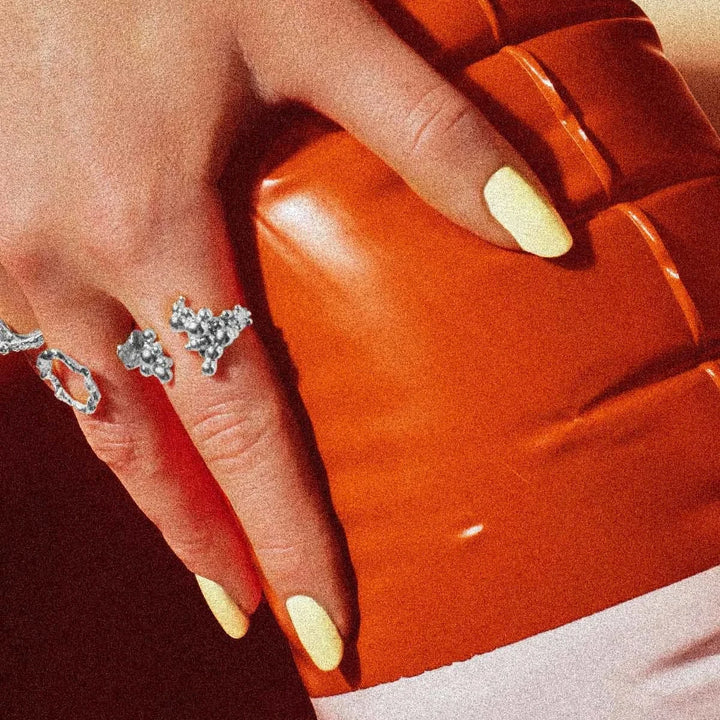 Vincent Orb Chronicles Solv Ring, elegant sølvring med organisk design på hånd med lyse negle foran orange baggrund. Model VJ163-URS-001-2