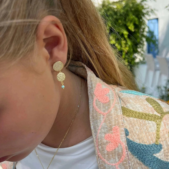 Sisse Marie ørestikker med gyldne plader og blå lapis perle vises båret udendørs, Model E-8804-GP.