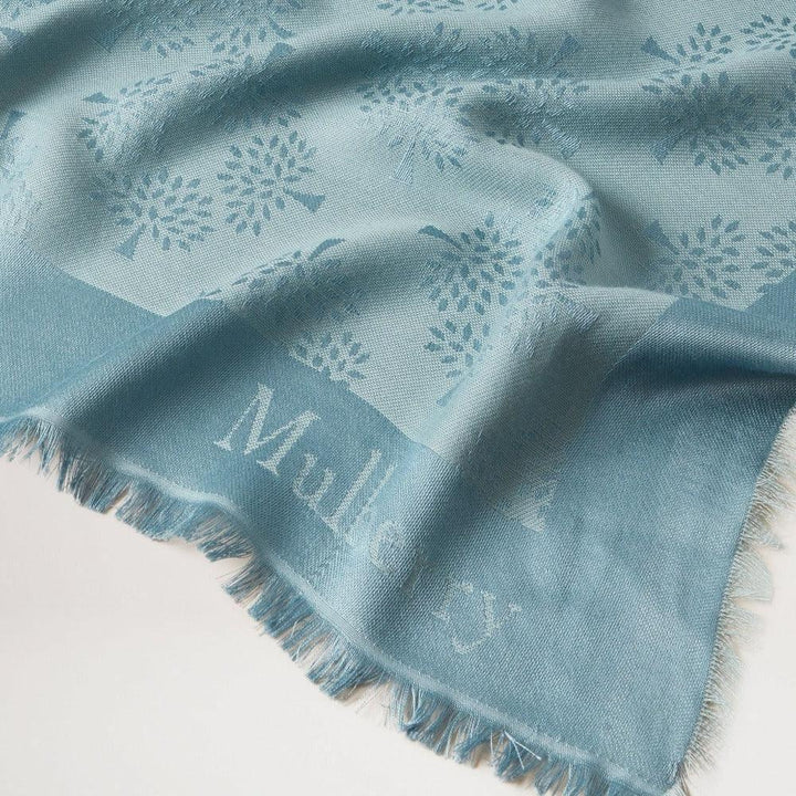 Mulberry Tree Square Silk Organic Cotton Cloud viser et blåt tørklæde med diskret træmønster. Model vs4639709d140