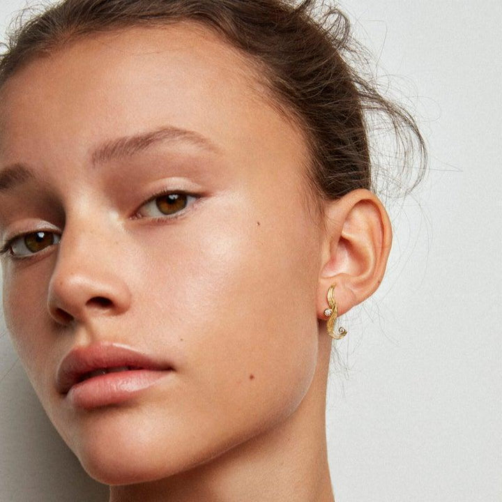 Polar Jewelry The Darning Needle forgyldt ørering på kvindes øre, elegant buet design. Model dan-st-l-gd-wz-00331-2