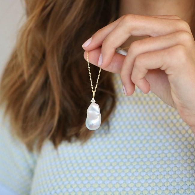 ro copenhagen 18kt fryd barok perle vedhæng diamanter vises i hånd mod mønstret trøje. Model 108637-2