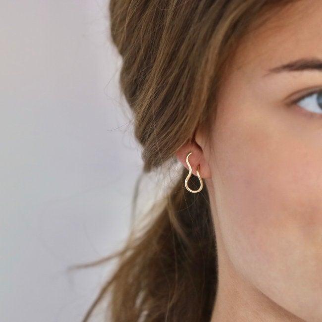 Ro Copenhagen 18kt Fryd Wave ørestik ses i venstre øre, elegant i bølgeformet guld. Model108102-2